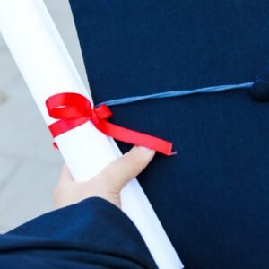 Close-up of a hand holding a diploma and graduation cap, symbolizing achievement.